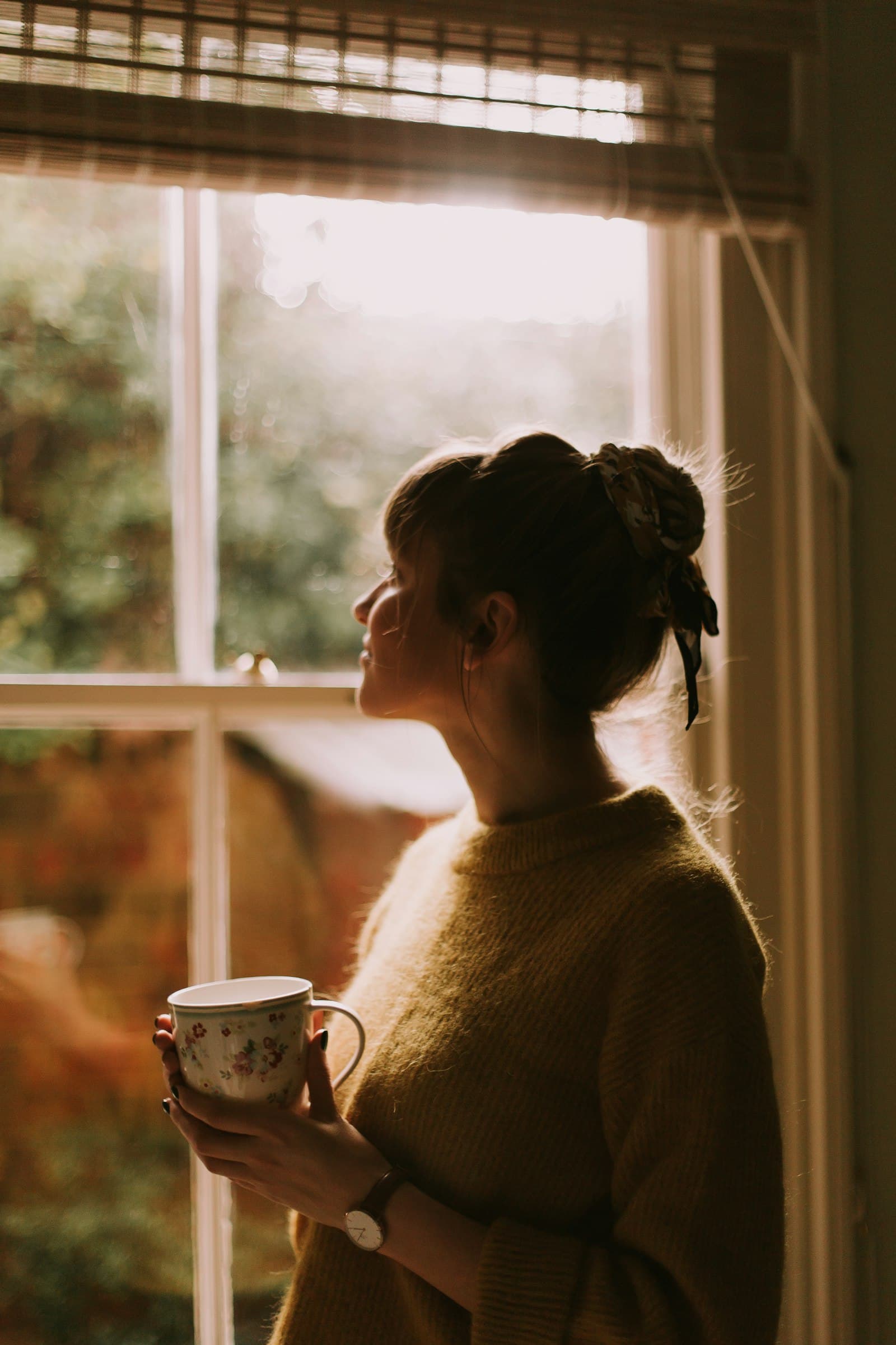 A woman holding a warm mug of tea by a sunlit window