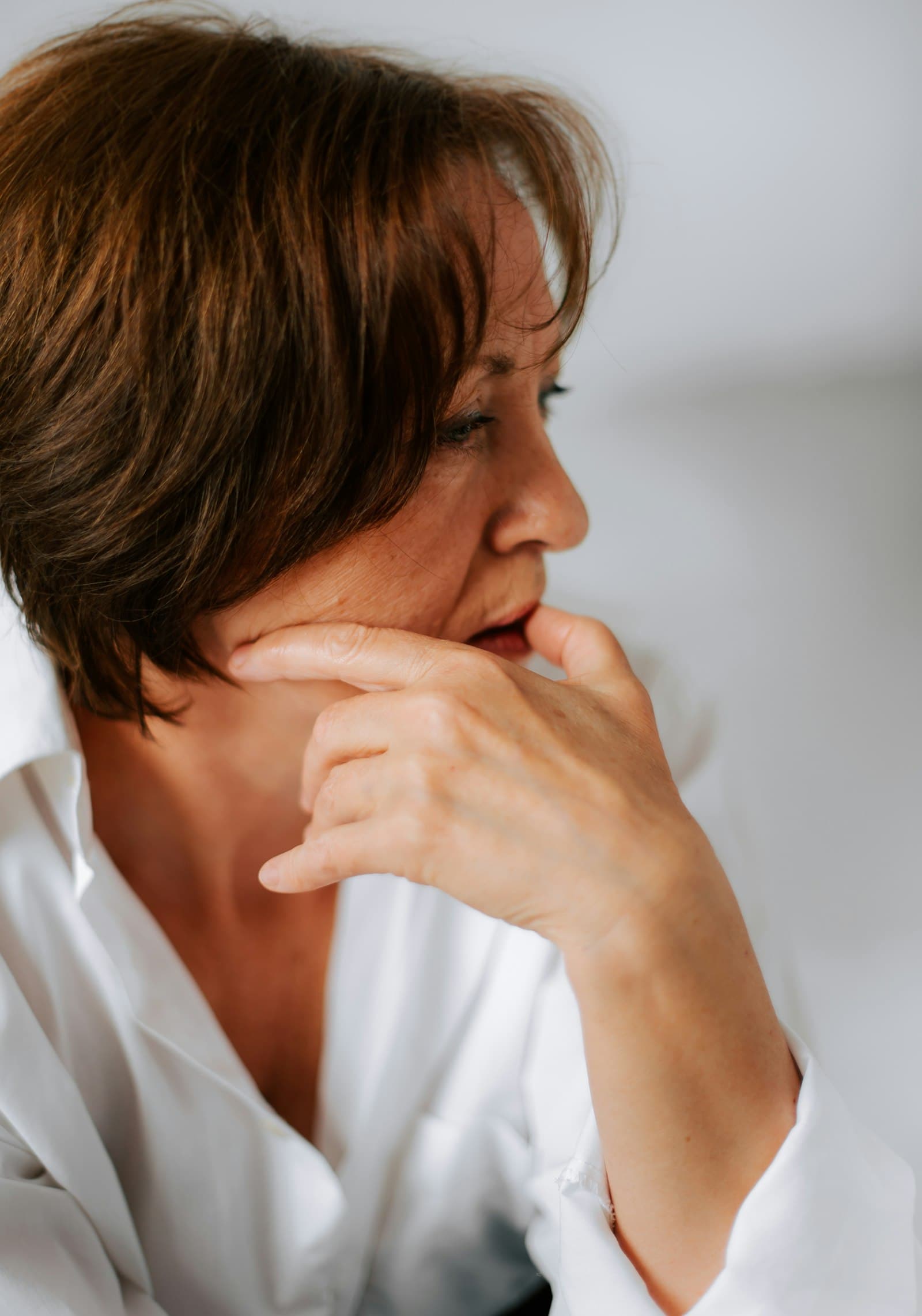 A woman in her 40s pausing thoughtfully, hand at her chin
