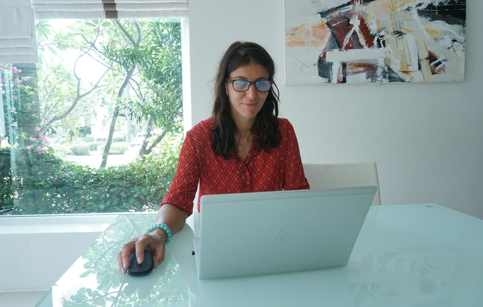 A woman working on a laptop at a bright table by a window