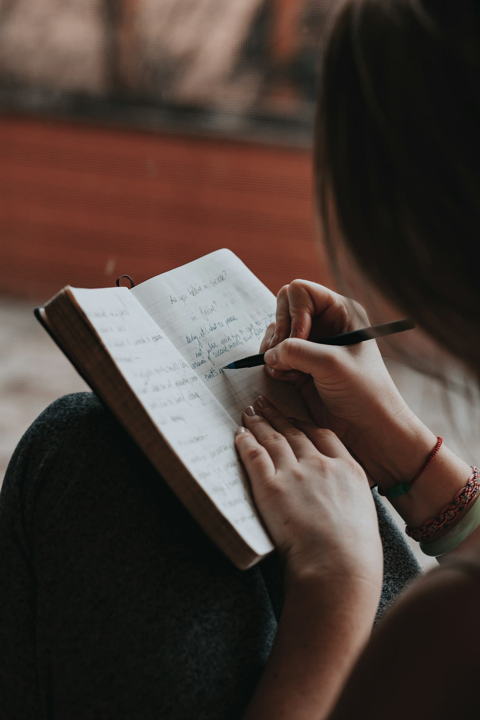 Close-up of hands writing in a notebook with a pen